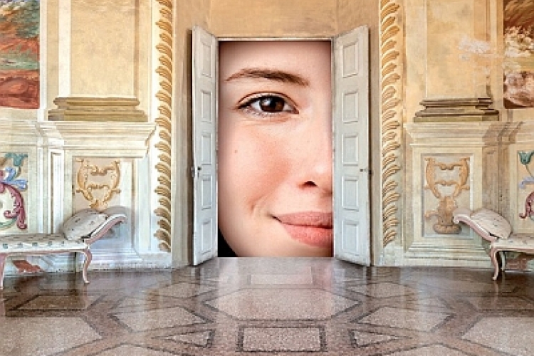 Foto di una stanza in stile con una porta aperta da cui si vede un viso di donna in primo piano che guarda con attraverso la porta con l'occhio aperto e sorride